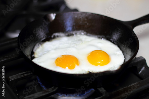 Two eggs frying sunny-side up in a cast iron pan on the stove.