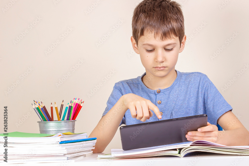 Kid sitting at table with books notebooks and using tablet computer Kid sitting at table with books notebooks and using tablet computer