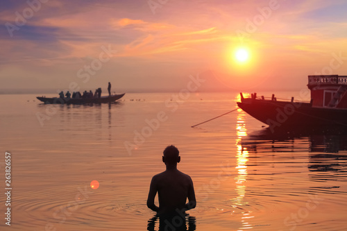 Old man meditates and offer prayers standing near the Ganges river bank at Varanasi at sunrise photo