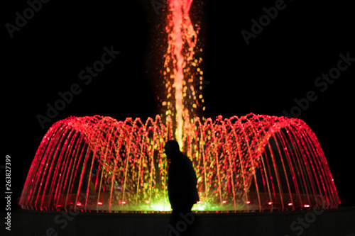 Silhouette of an old man in front of fountain with colored illumination photo