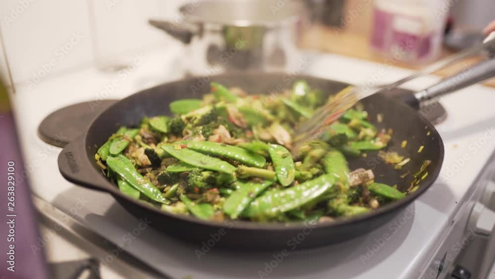 Woman cooking wok with mushrooms, brocolli, chili, noodles, leek, suger peas and soy.