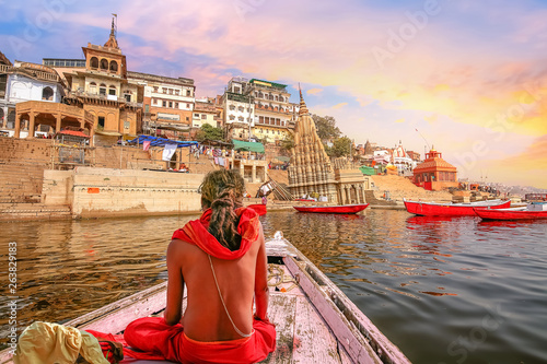 Tableau sur toile Varanasi city architecture with Ganges river bank at sunset with view of Hindu sadhu enjoying a boat ride on river Ganga