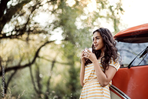 A young girl with coffee by a car on a roadtrip through countryside. photo