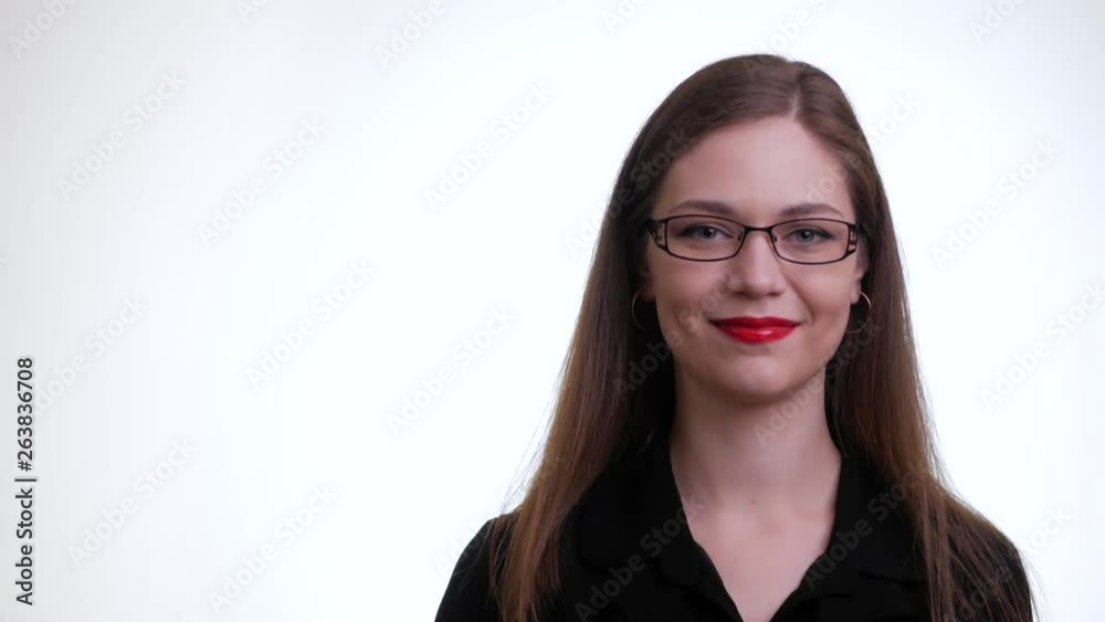 Young beautiful woman in glasses looks at camera and winks on a white background. Portrait of pretty brunette girl in a black shirt, isolated over white background in studio. Concept of emotions. Young beautiful woman in glasses looks at camera and winks on a white background. Portrait of pretty brunette girl in a black shirt, isolated over white background in studio. Concept of emotions.