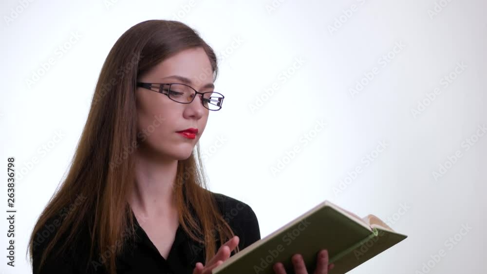 Concentrated brunette woman in a black shirt and eyeglasses reading book over white background Concentrated brunette woman in a black shirt and eyeglasses reading book over white background