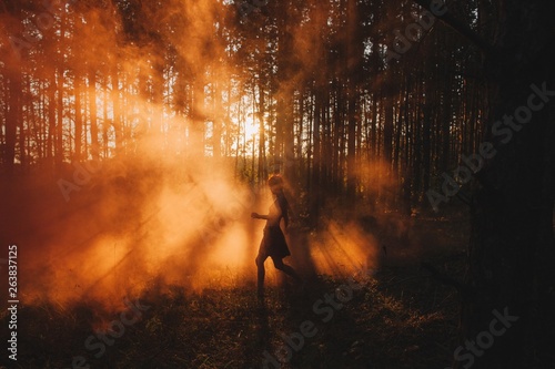 Silhouette of girl walking by fog in sunset light in pine forest
