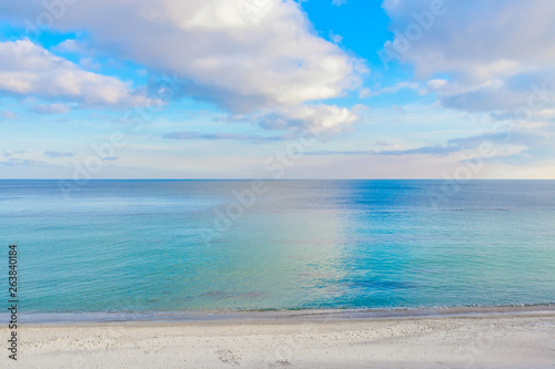 Contrast photograph of the sea and cloudy sky. Clouds reflected in water. Footprints on coastal sand