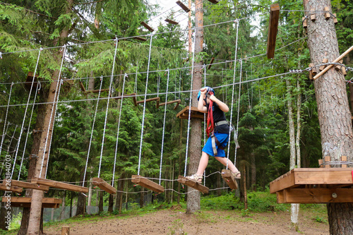 boy has challenge in an adventure park, he walking high up the rope swing track (trail)