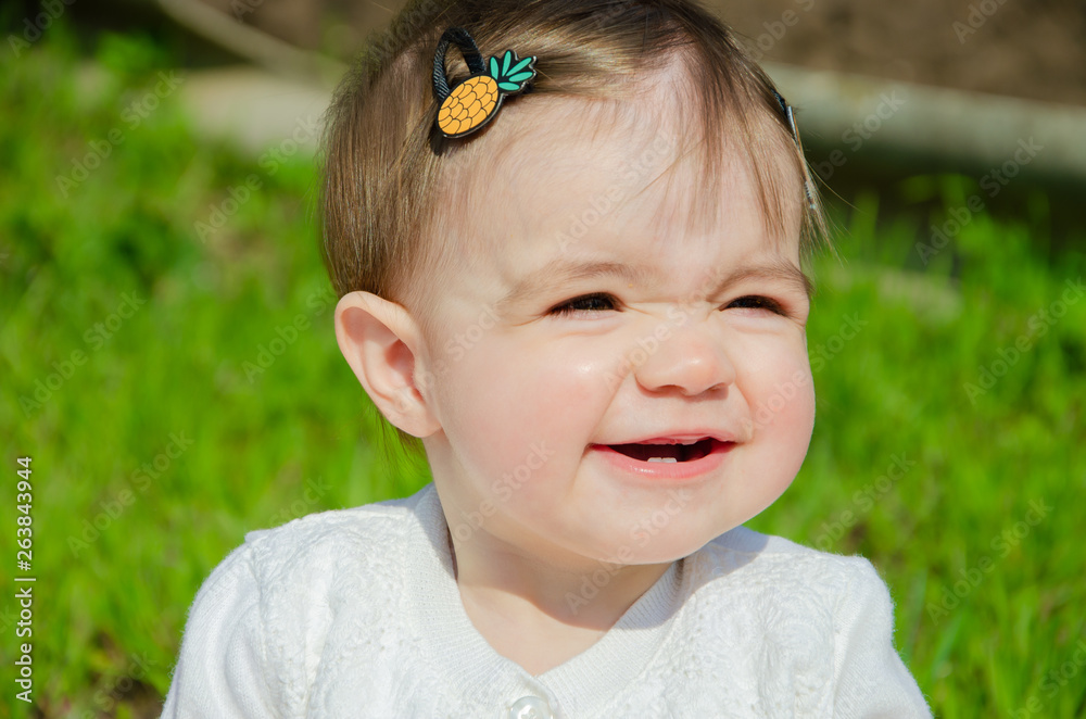 Baby in bright clothes on a pink plaid on green grass in the park. Newborn baby outside on a warm day. Little girl plays on a plaid on a green lawn in spring