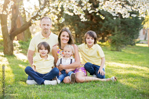 Beautiful family, mother, father and three kids, boys, having familly outdoors portrait taken on a sunny spring evening, beautiful blooming garden, sunset time © Tomsickova
