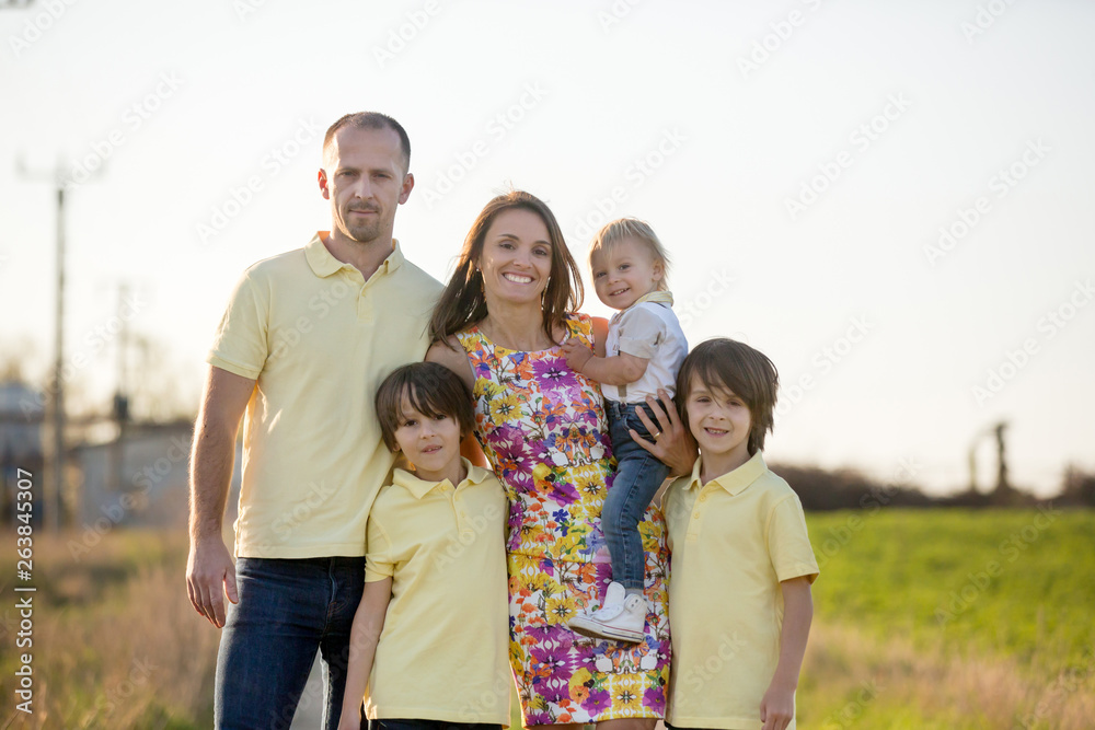 Beautiful family, mother, father and three kids, boys, having familly outdoors portrait taken on a sunny spring evening, beautiful blooming garden, sunset time Beautiful family, mother, father and three kids, boys, having familly outdoors portrait taken on a sunny spring evening, beautiful blooming garden, sunset time