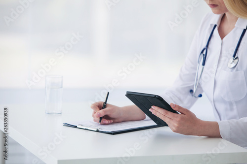 Female caucasian doctor using tablet and writing diagnosis in medical forms documents.  Close up