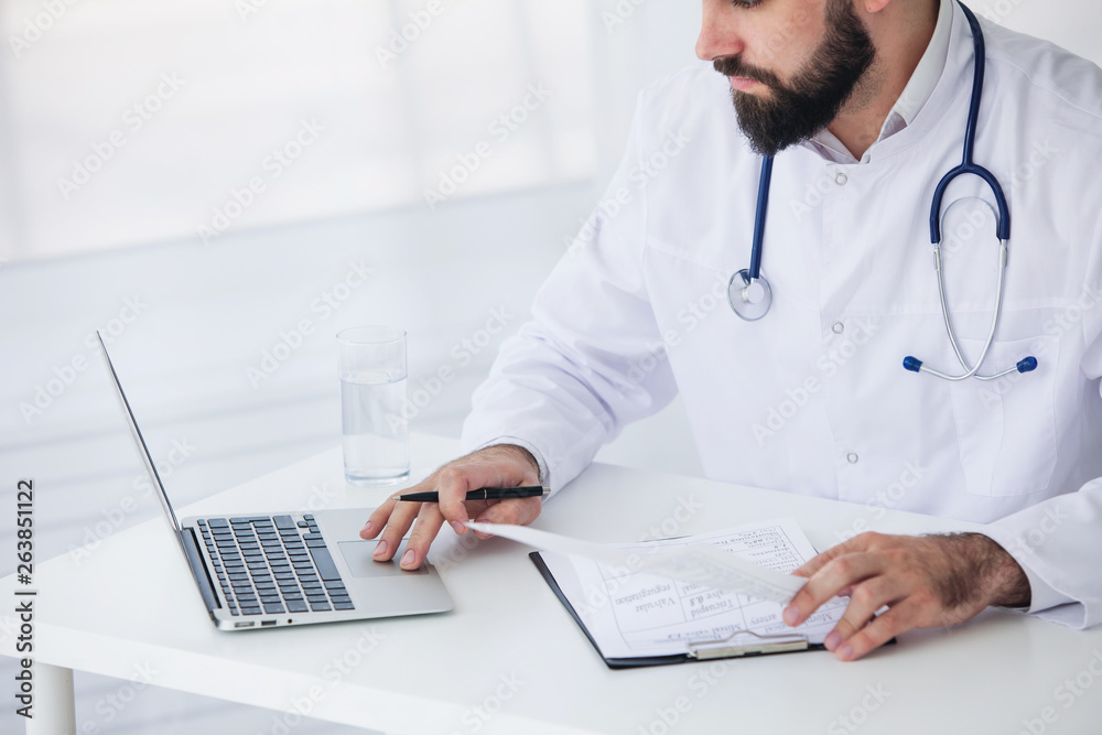 Doctor is working with documents and laptop in his medical office. Close up Doctor is working with documents and laptop in his medical office. Close up