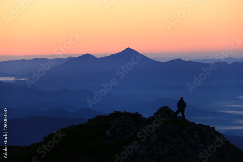 東北飯豊山　山頂直下本山小屋から　登山者シルエットと朝焼けに煙る会津磐梯山 © DONDON2018