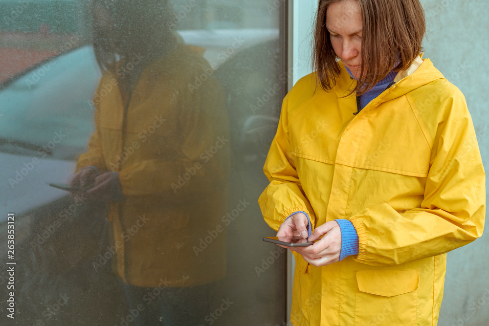 Woman in yellow raincoat texting on mobile phone outdoors Woman in yellow raincoat texting on mobile phone outdoors