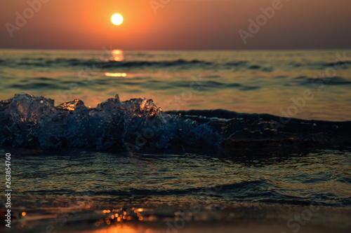 Fototapeta Naklejka Na Ścianę i Meble -  sunrise at the shore of the sea and ocean, seen from the sand level, with the glowing wave of water, and pleasant bokeh