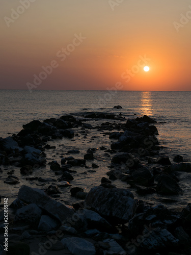 sunrise at the seashore  among the rocks coming out of the water  with orange sun