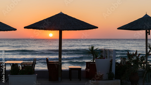 sunrise on the seafront with reed sun silhouette umbrellas  the sea with waves and dinner table.