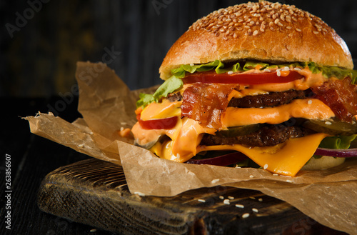 Cheeseburger with Two Beef Patties, Cheddar Cheese, Bacon, Iceberg Lettuce, Sliced Tomatoes and Red Onion on Cutting Board.