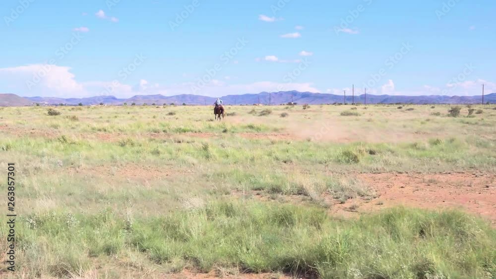 Cowboy riding horse off into the distance through dry dusty plains of Texas Cowboy riding horse off into the distance through dry dusty plains of Texas