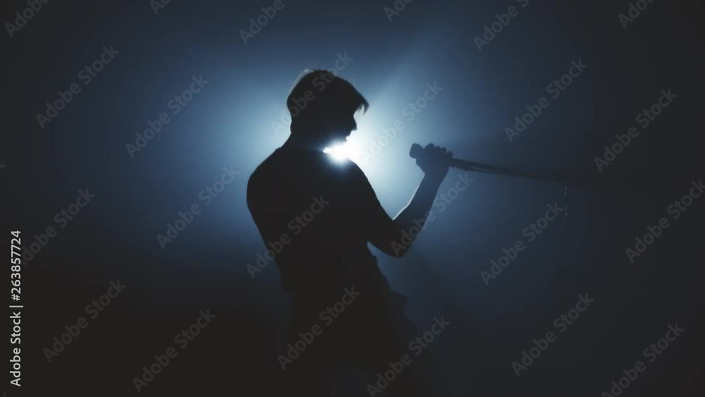 Man singer in the smoke and light sings into a microphone and dance. Dark background. Silhouette