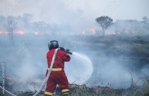Closeup of firefighter in red uniform doing his work to control extensive fire in agricultural field. 
