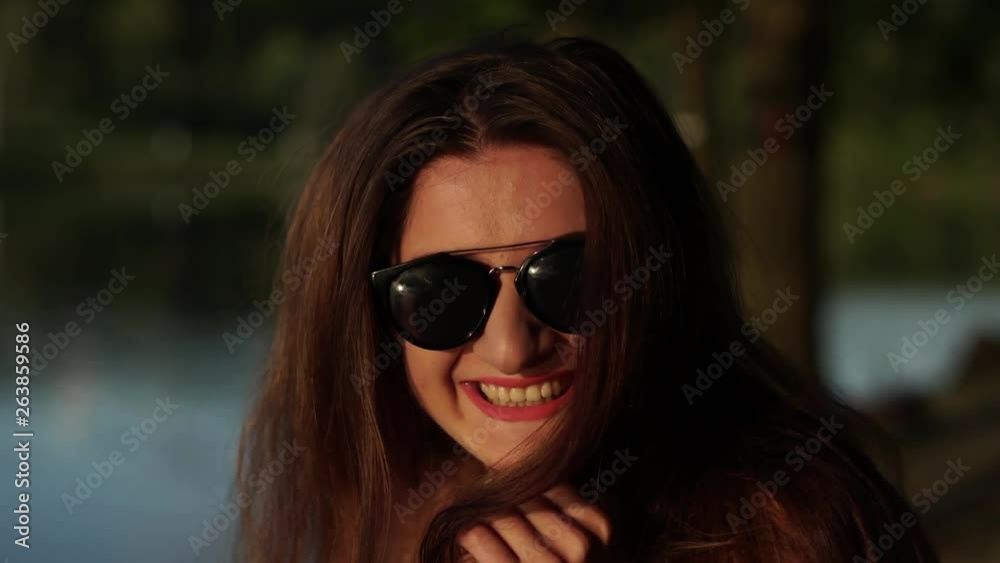 Brunette in a white strapless dress and sunglasses looking in the camera and then whirling on a bokeh summer nature background Brunette in a white strapless dress and sunglasses looking in the camera and then whirling on a bokeh summer nature background