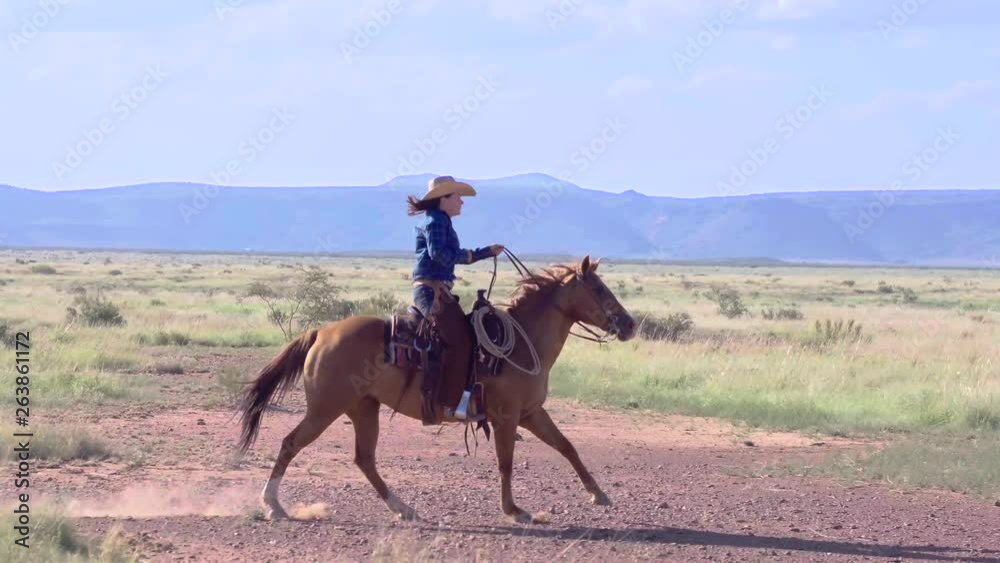 Side profile of Cowgirl Rancher riding horseback through wide open plains Side profile of Cowgirl Rancher riding horseback through wide open plains