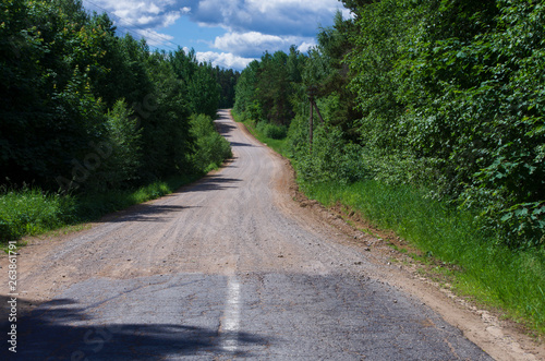 Summer landscape with the end of the asphalt road and the beginning of the gravel road through a dense forest