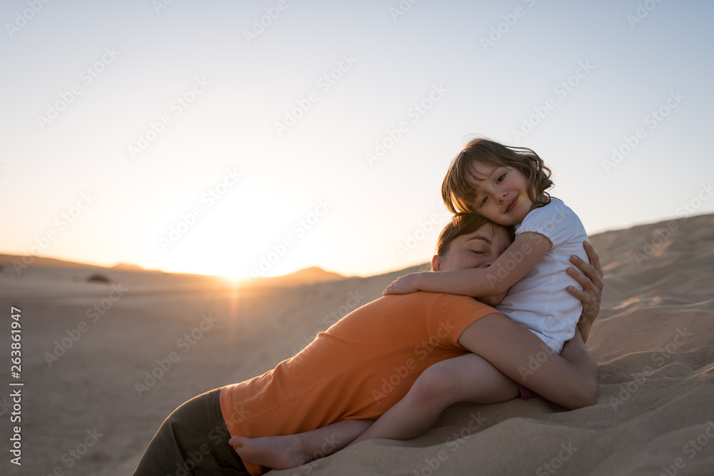 Mother laying on sand dune and hugging with her daughter