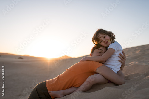 Mother laying on sand dune and hugging with her daughter