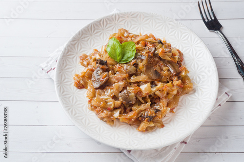 Stewed cabbage with mushrooms on white wooden background
