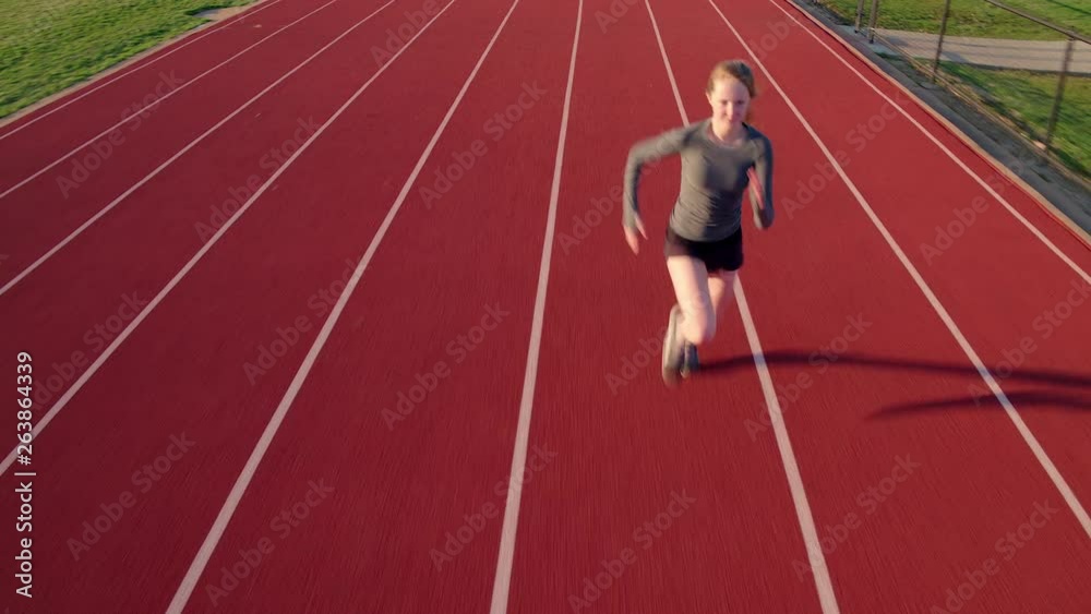 Teen girl athlete sprints on a high school track aerial camera preceding Teen girl athlete sprints on a high school track aerial camera preceding