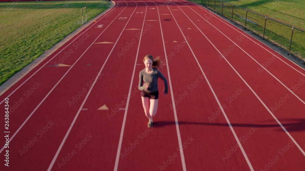 Teen girl runs on a high school track drone camera precedes