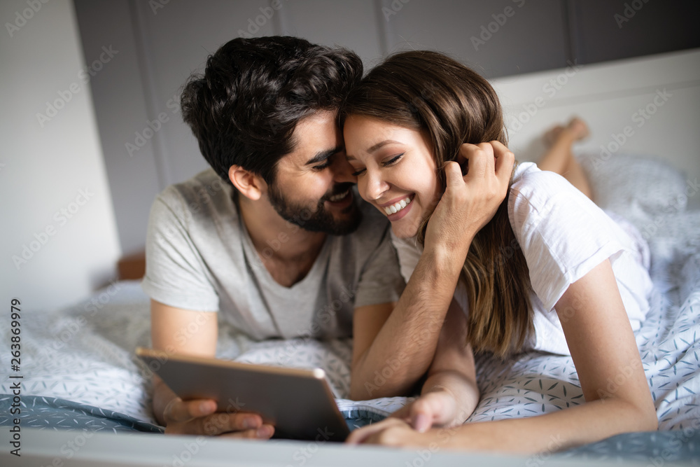Happy couple in love using tablet in pajamas at home Happy couple in love using tablet in pajamas at home