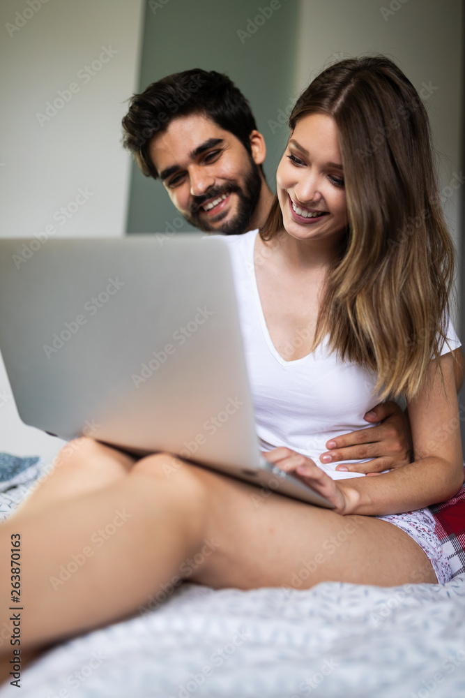 Young couple relaxing on bed with laptop. Love, technology, happiness, people and fun concept.