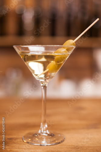 Delicious martini drink with green olives on stick over a wooden bar counter