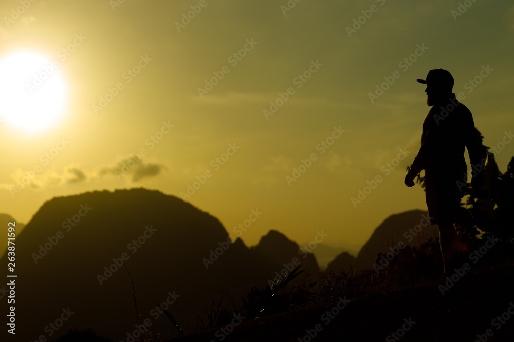 A young photographer with a beard and a cap meets the dawn on a high mountain.