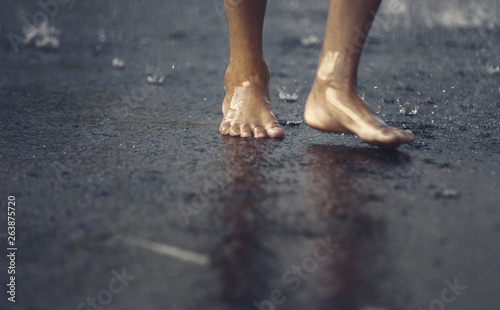 Boy's bare feet walking under the rain.Low angle view.