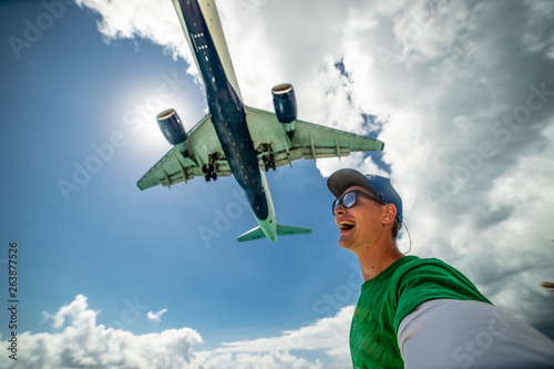 Smiling guy taking selfie with airplane flying over on famous Maho beach. Concept of vacation and traveling photo