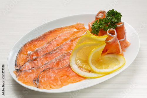 salted red fish slices laid out on a plate, salmon or trout, decorated with parsley and lemon slices
