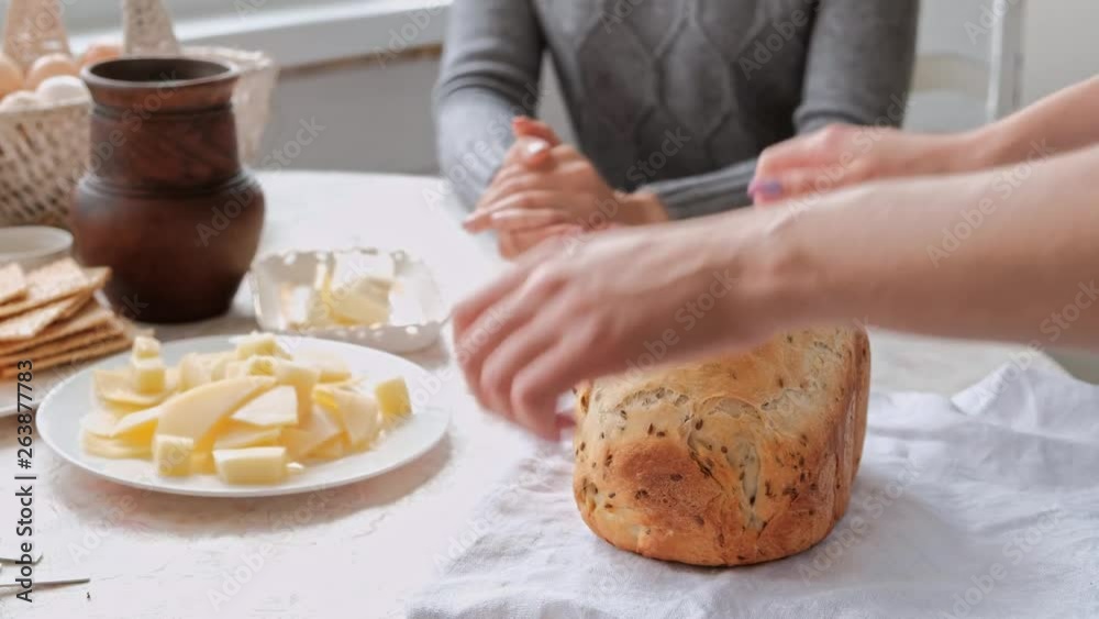 Home owner wife treats guests and the family with wheat bread, just baked. Kitchen and dining room in country house. Slices bread with a knife. Home owner wife treats guests and the family with wheat bread, just baked. Kitchen and dining room in country house. Slices bread with a knife.
