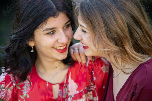 Close up of two female friends, one blonde and the other brunette are smiling cheerfully. Concept of friendship and complicity of Caucasian girls.