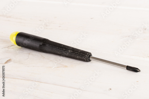 One whole screwdriver with a yellow black plastic handle work item on white wood