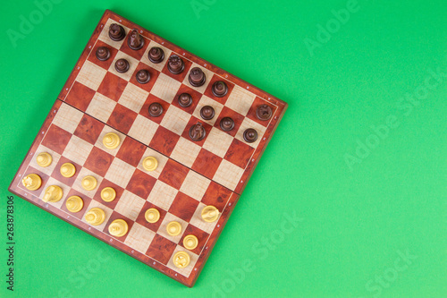 Chessboard with chesses on light green background, top view
