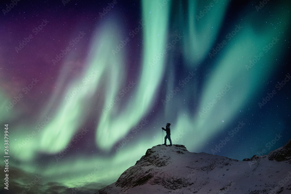Man climber standing on snowy peak with aurora borealis and starry