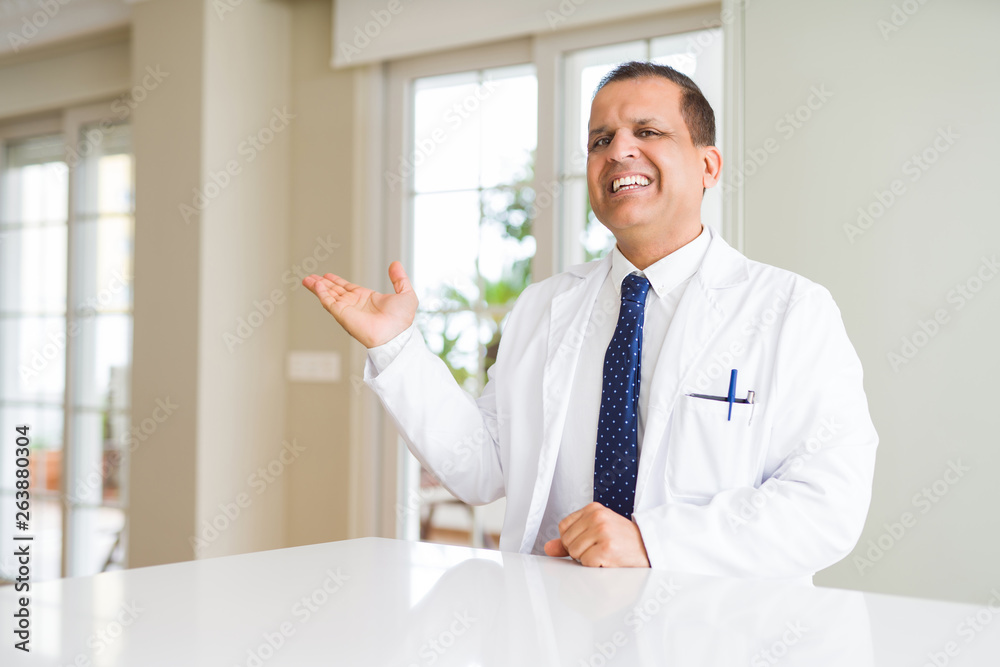 Middle age doctor man wearing medical coat at the clinic smiling cheerful presenting and pointing with palm of hand looking at the camera.