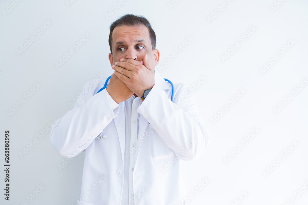 Middle age doctor man wearing stethoscope and medical coat over white background shocked covering mouth with hands for mistake. Secret concept. Middle age doctor man wearing stethoscope and medical coat over white background shocked covering mouth with hands for mistake. Secret concept.