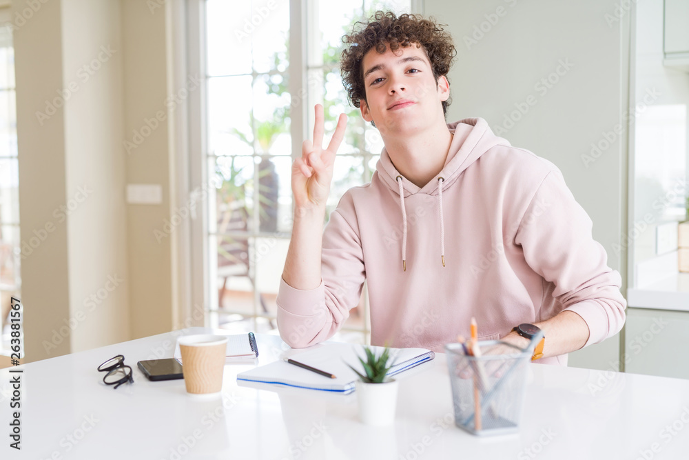 Young student man writing on notebook and studying smiling with happy face winking at the camera doing victory sign. Number two. Young student man writing on notebook and studying smiling with happy face winking at the camera doing victory sign. Number two.