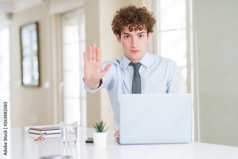 Fototapeta premium Young business man working with computer laptop at the office doing stop sing with palm of the hand. Warning expression with negative and serious gesture on the face.